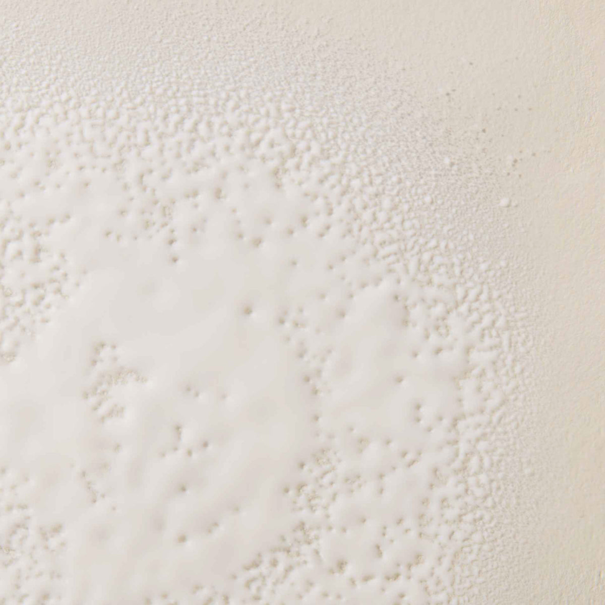Nahaufnahme des Living Proof No Frizz Smooth Styling Spray als feine weiße Sprühtropfen auf einer glatten, cremefarbenen Oberfläche.