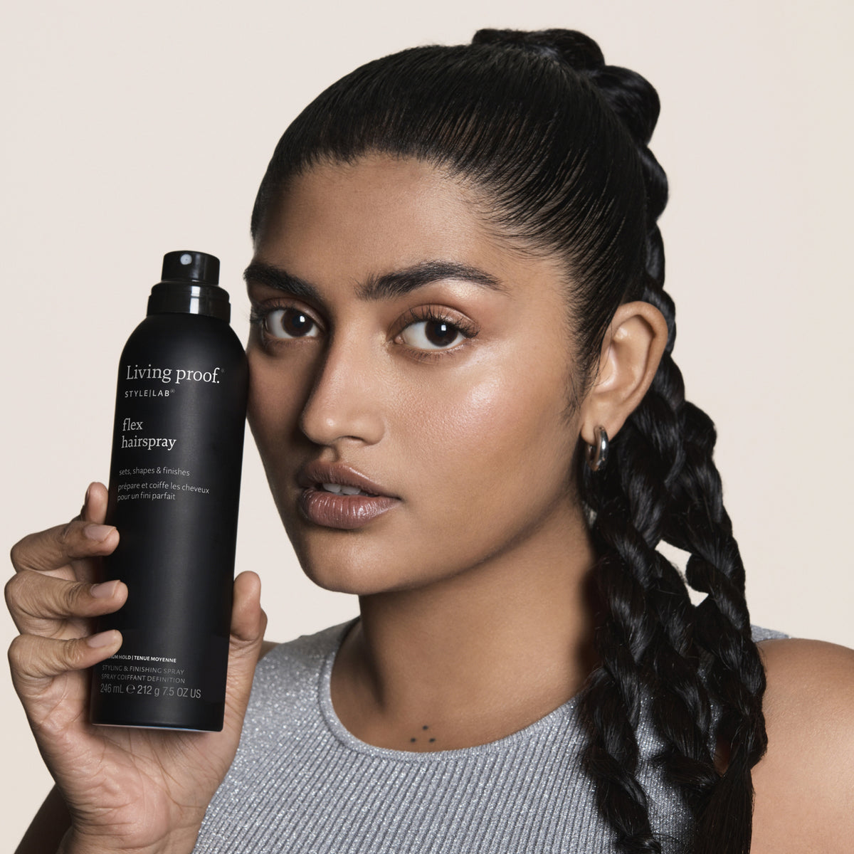 Eine Frau mit geflochtenem Zopf hält eine schwarze Living Proof Style Lab Flex-Hairspry Flasche neben ihr Gesicht.