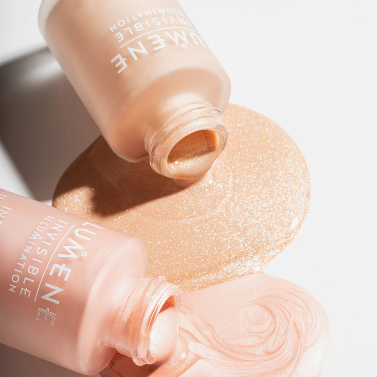 Zwei geöffnete Flaschen Lumene INVISIBLE ILLUMINATION Illuminizer, wobei das Produkt auf eine weiße Fläche verschüttet wurde.