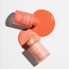 Zwei Flaschen Lumene INVISIBLE ILLUMINATION Liquid Blush in Rosa- und Korallentönen mit verschütteter Flüssigkeit auf weißem Hintergrund.