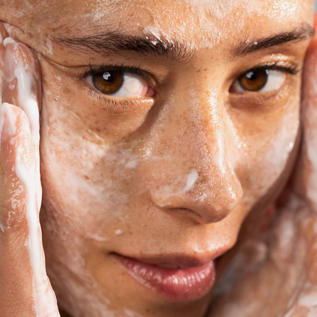 Eine Frau reinigt ihr Gesicht mit Lumene Nordic-C [VALO] Exfoliating Gel Cleanser, die Hände umrahmen ihr Gesicht in einer Nahaufnahme.