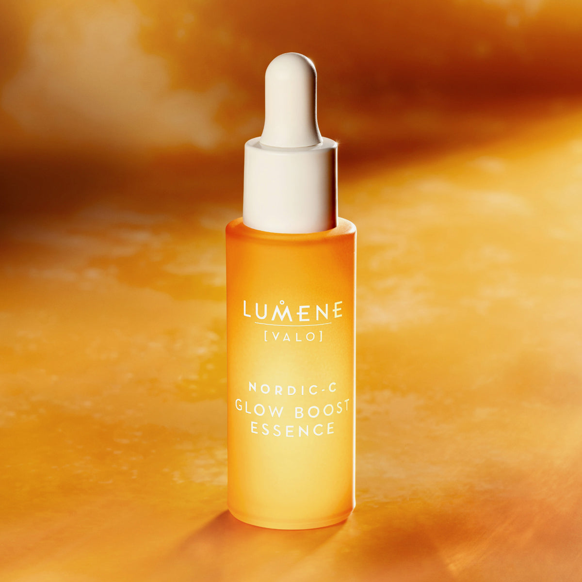 Oranges Fläschchen Lumene NORDIC-C [VALO] Glow Boost Essence mit weißem Tropfverschluss auf einem orangefarbenen Hintergrund.