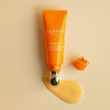 Eine orangefarbene Tube Lumene NORDIC-C [VALO] Glow Boost Eye Serum mit Creme und einer Moltebeere, dargestellt auf einem beigen Hintergrund.