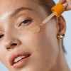 Eine Frau trägt das NORDIC-C [VALO] Triple Glow Serum von Lumene mit einer Pipette auf ihre Wange und zeigt eine strahlende, gesunde Haut.
