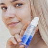 Blonde Frau lächelt, während sie eine Flasche Lumene NORDIC HYDRA [LAHDE] Moisturizing Prebiotic Oil-Cocktail an ihr Gesicht hält.