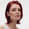 Selbstbewusste Frau mit kurzen, glatten roten Haaren präsentiert maria nila Finishing Spray vor einem weißen Hintergrund.