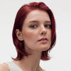 Eine selbstbewusste Frau mit kurzem, glattem, rotem Haar und heller Haut posiert vor einem schlichten Hintergrund und präsentiert ihre leuchtende Farbe mit maria nila Luminous Colour Shampoo.