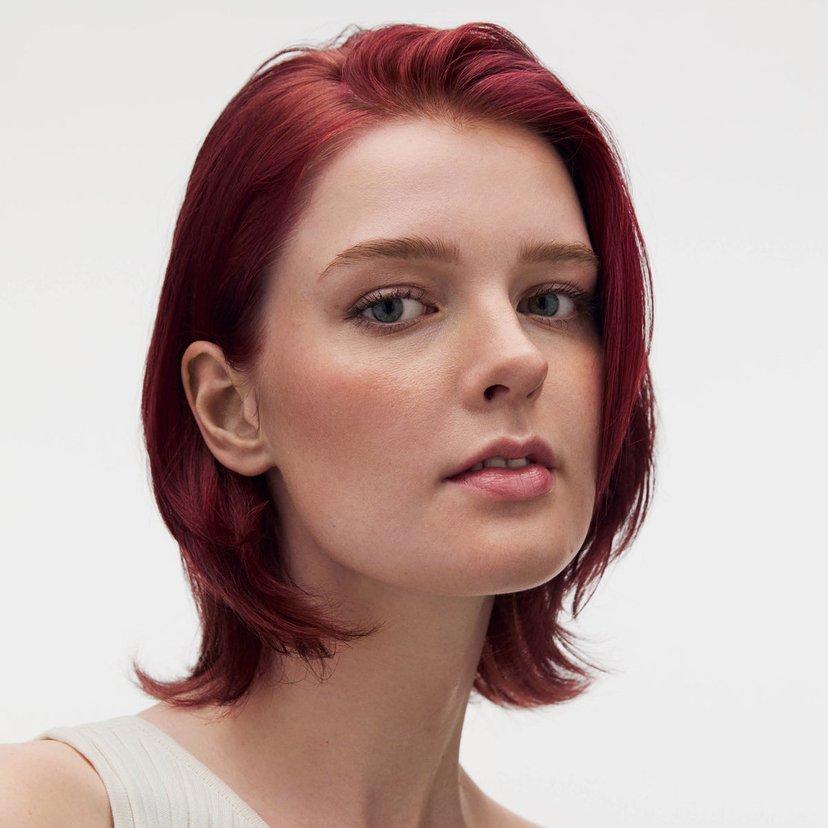 Eine selbstbewusste Frau mit kurzem, glattem, rotem Haar und heller Haut posiert vor einem schlichten Hintergrund und präsentiert ihre leuchtende Farbe mit maria nila Luminous Colour Shampoo.