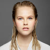 Eine junge blonde Frau präsentiert langes, nasses Haar nach Anwendung des Sheer Silver Shampoo von maria nila.