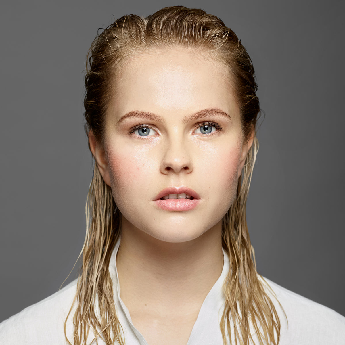 Eine junge blonde Frau präsentiert langes, nasses Haar nach Anwendung des Sheer Silver Shampoo von maria nila.
