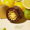 Offenes Glas Deep Vita C Capsule Cream mit gelben Kapseln, umgeben von frischen Zitronen und Limetten auf einer hellen Oberfläche.