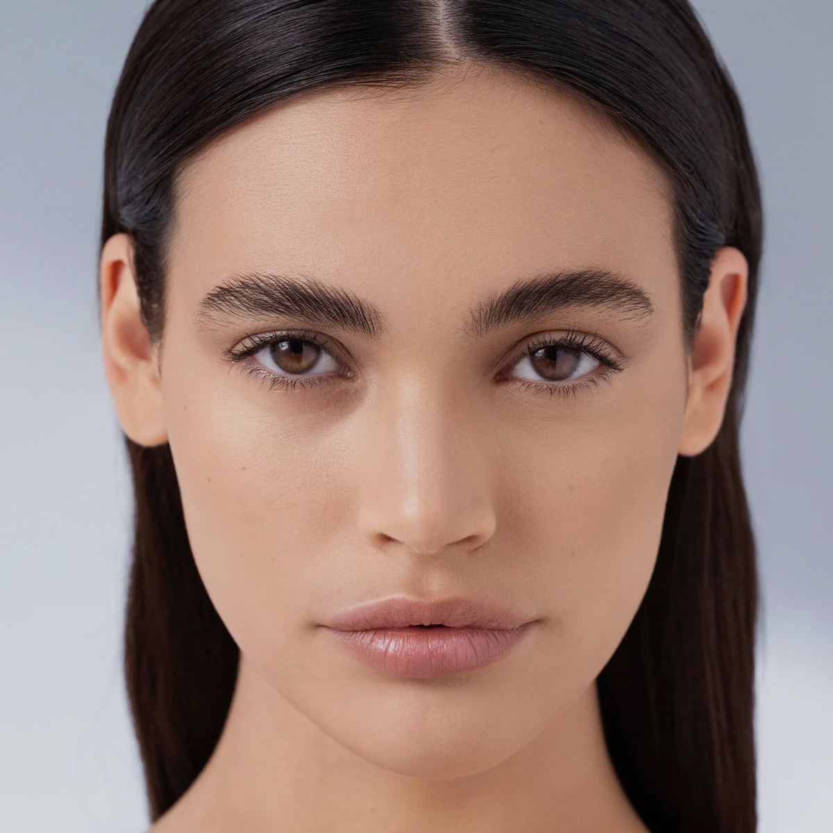 Eine Frau mit glattem dunklem Haar, neutralem Make-up und einem ruhigen Gesichtsausdruck blickt direkt in die Kamera und präsentiert den Chrono Flawless Primer von Mesauda Beauty.