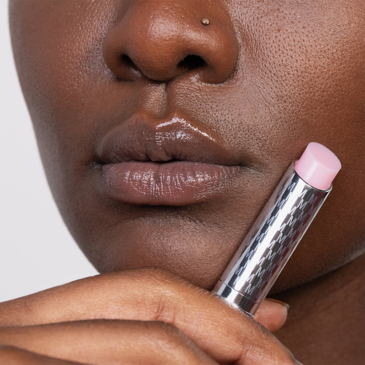 Eine Person mit glänzenden Lippen hält eine silberne Tube des Lippenbalsams THE HYDRAMORPHOSIS TWIN SET von Mesauda Beauty an ihren Mund.