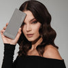 Eine Frau mit welligem dunklem Haar hält die ARCHETYPE II Palette neben ihrem Gesicht und trägt ein schulterfreies schwarzes Top.