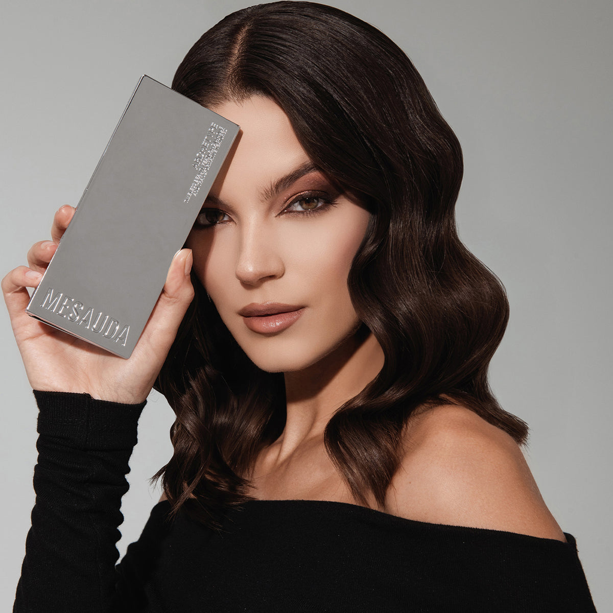 Eine Frau mit welligem dunklem Haar hält die ARCHETYPE II Palette neben ihrem Gesicht und trägt ein schulterfreies schwarzes Top.