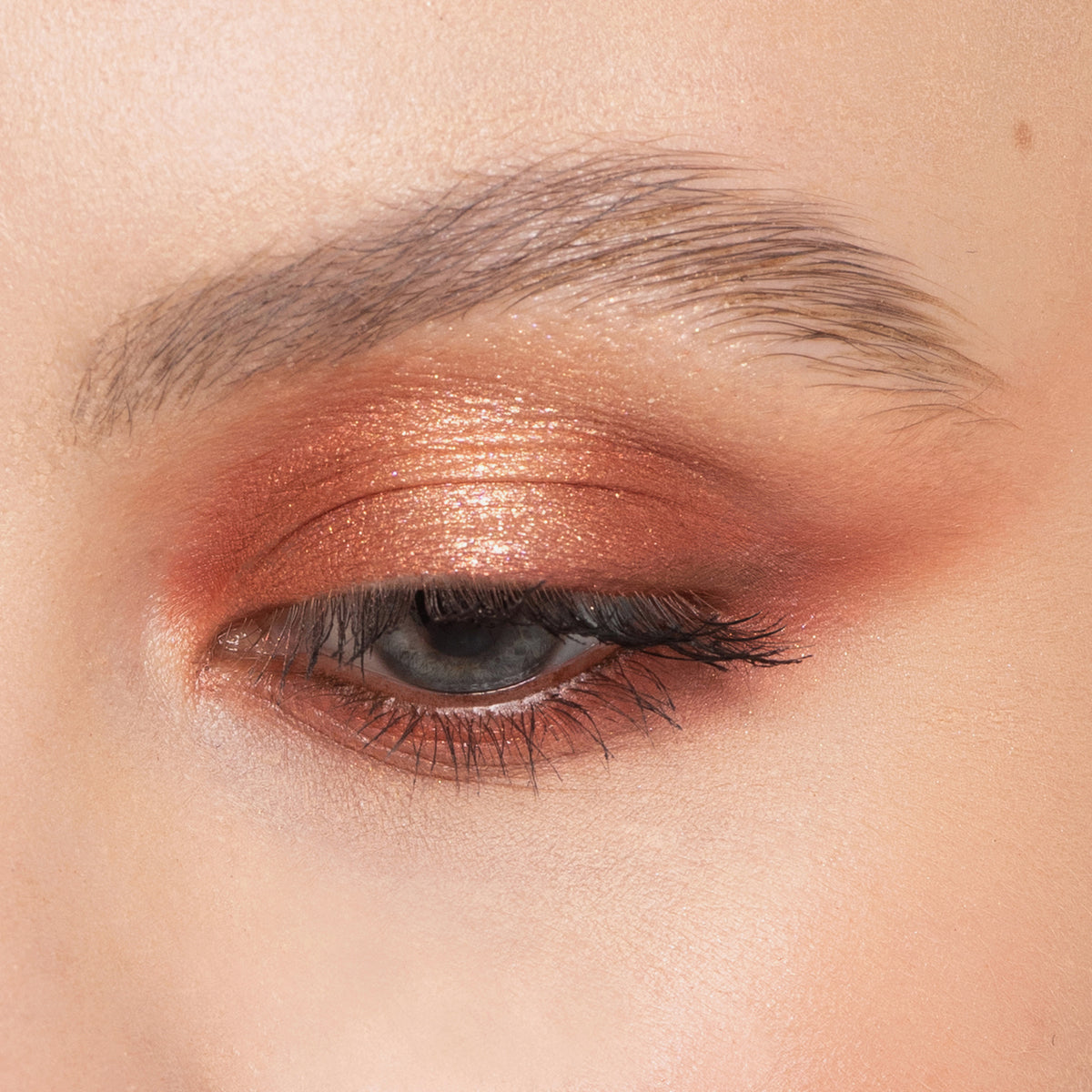 Nahaufnahme eines geschlossenen Auges mit schimmerndem Kupferlidschatten und definierter Augenbraue, mit Bare Harmony 3.0 von Mesauda Beauty.