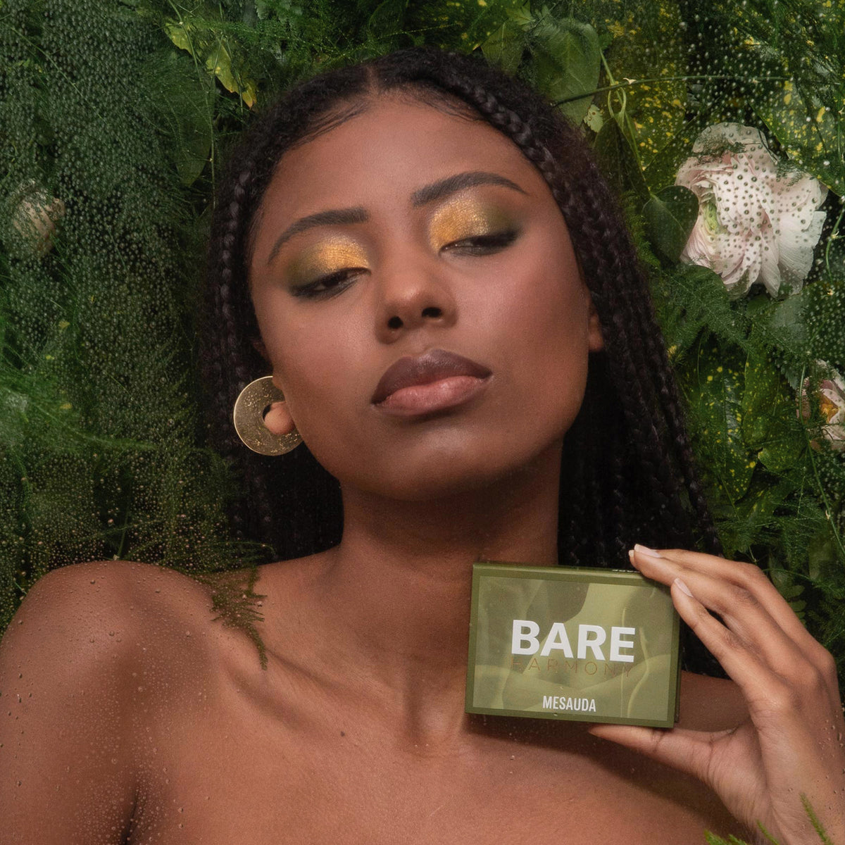Eine Frau mit geflochtenem Haar hält die grüne Bare Harmony 3.0 Lidschattenpalette von Mesauda Beauty in der Hand und posiert vor einem floralen Hintergrund.