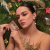 Eine Frau mit kräftigem Make-up hält die Mesauda Beauty Bare Harmony 3.0 Palette in der Hand, umgeben von Blumen und Grünzeug.