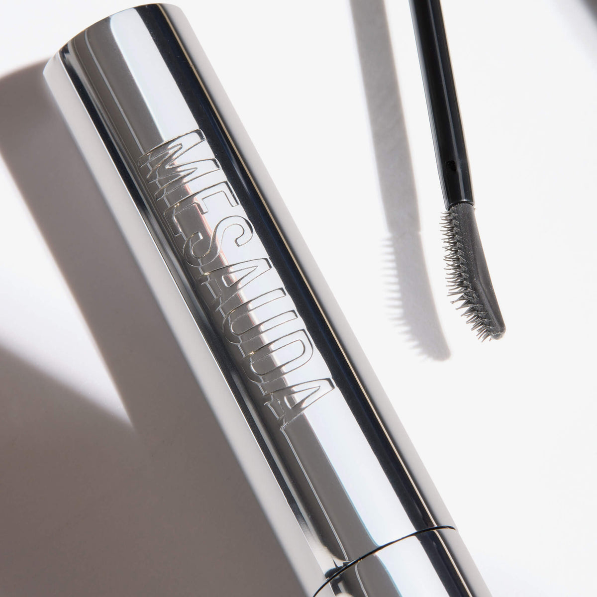 Eine silberne Mesauda Beauty Brow Glaminate - 101 Clear Tube mit einem gebogenen Borstenkopf daneben auf weißem Hintergrund.