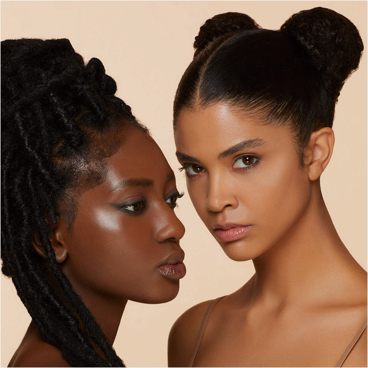 Zwei Frauen mit strahlender Haut und gestyltem Haar posieren eng beieinander vor einem neutralen Hintergrund und präsentieren ihr strahlendes Aussehen mit Dew Shield von Mesauda Beauty.