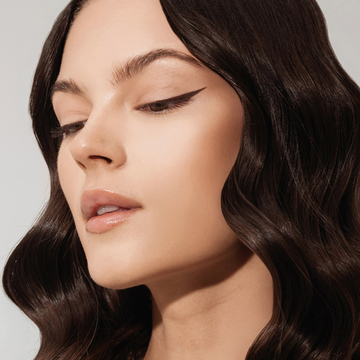 Eine Frau mit welligem Haar und einem Winged-Eyeliner-Look mit dem Ink Liner Brownie vor einem hellen Hintergrund.