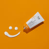 Eine Tube Hypershield®️ Tagespflege mit UVA-/UVB-Schutz, die ein lächelndes Gesicht auf einem leuchtend orangefarbenen Hintergrund bildet.