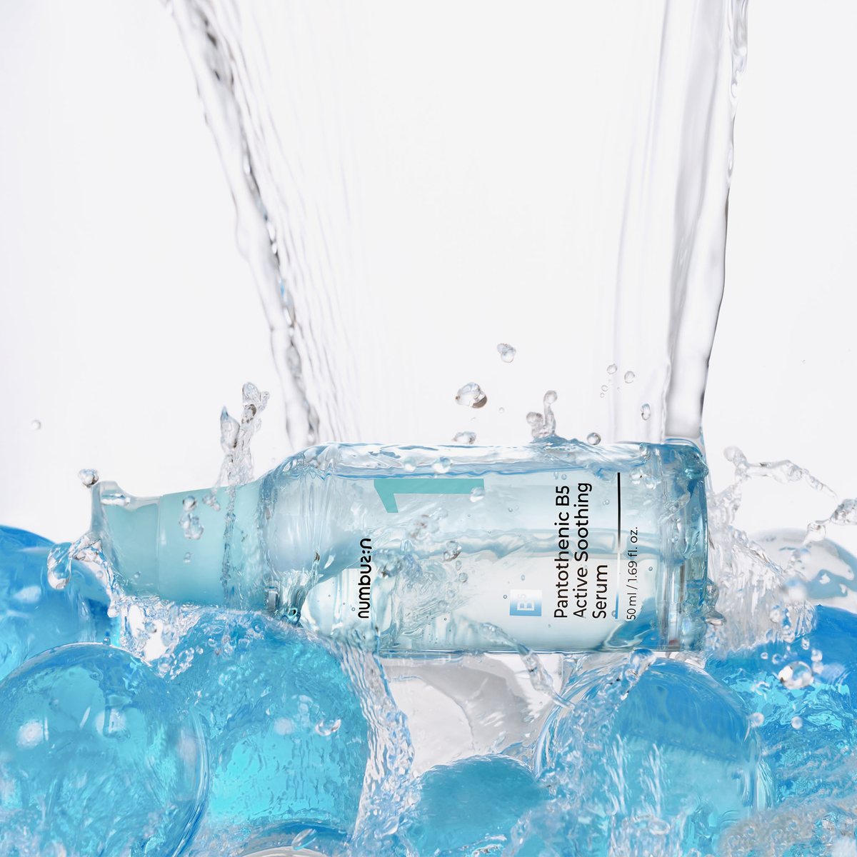 Das No.1 Pantothenic B5 Active Soothing Serum von numbuzin ruht auf blauen Gelkugeln, über die sich das Wasser ergießt.