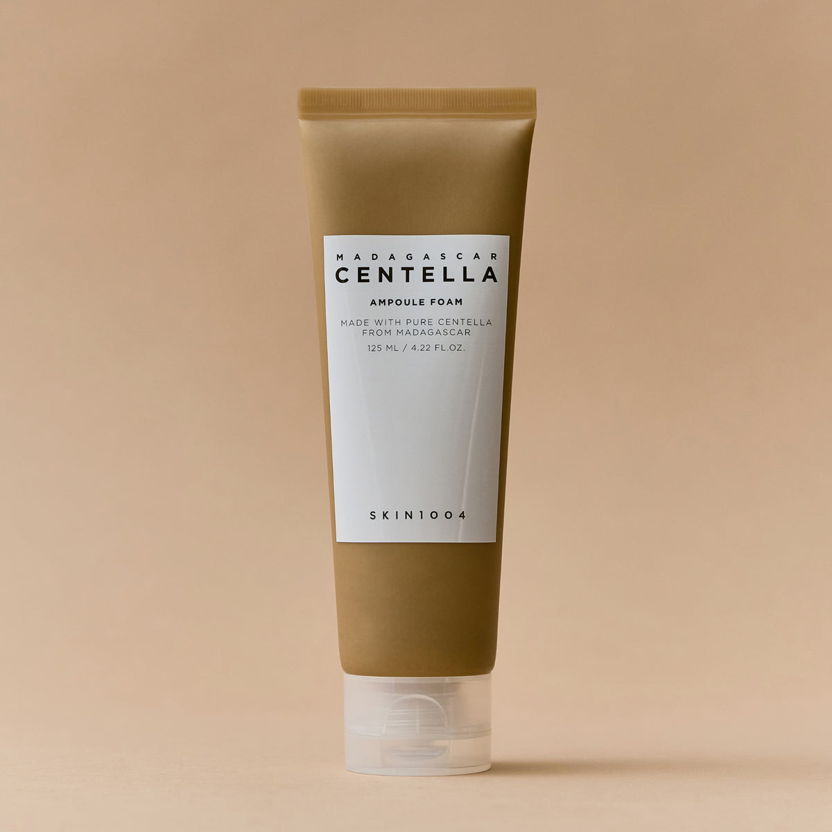 Eine Tube Madagascar Centella Ampoule Foam vor einem beigen Hintergrund.