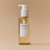 Eine durchsichtige Flasche Madagascar Centella Light Cleansing Oil mit weißem Pumpverschluss steht vor einem beigen Hintergrund.