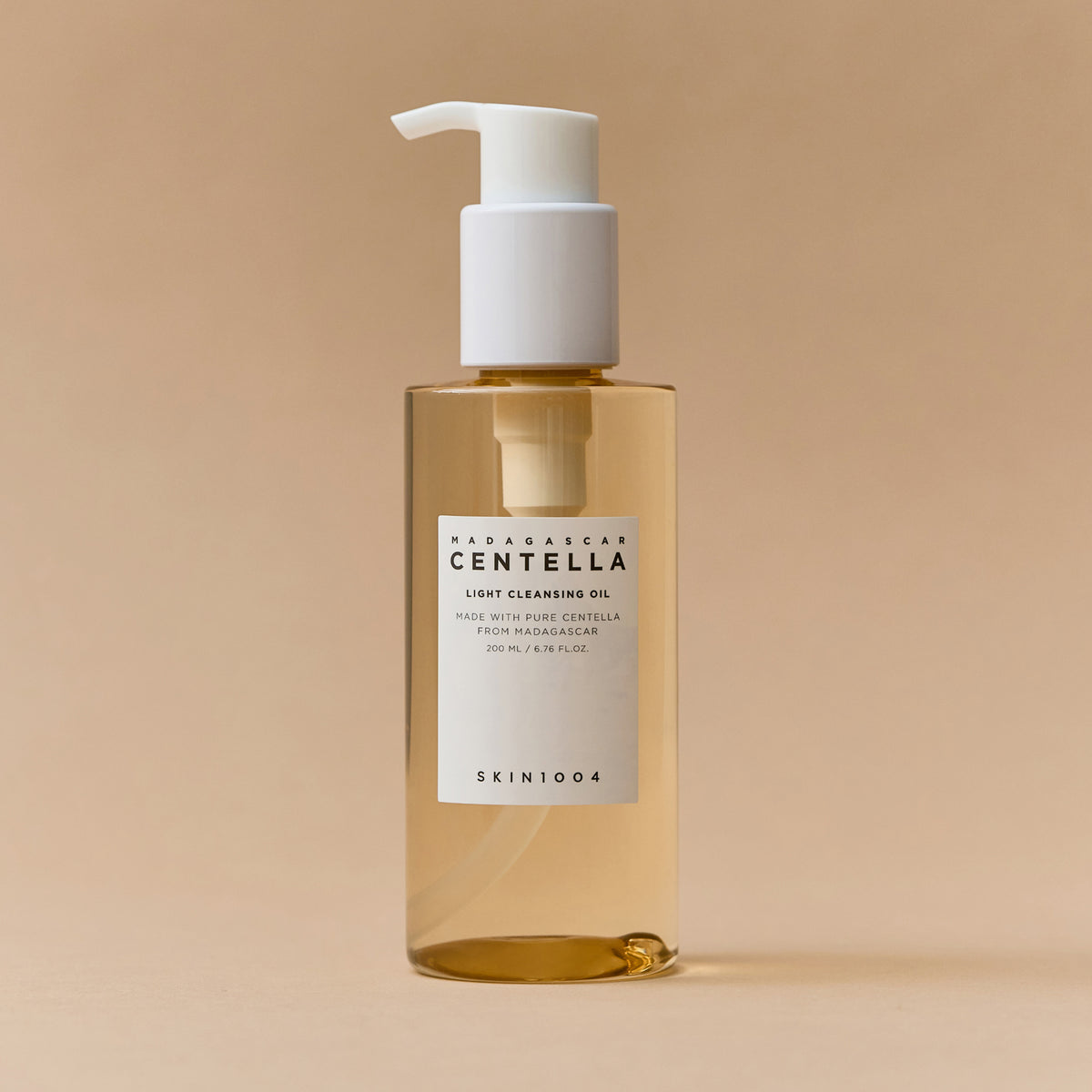 Eine durchsichtige Flasche Madagascar Centella Light Cleansing Oil mit weißem Pumpverschluss steht vor einem beigen Hintergrund.