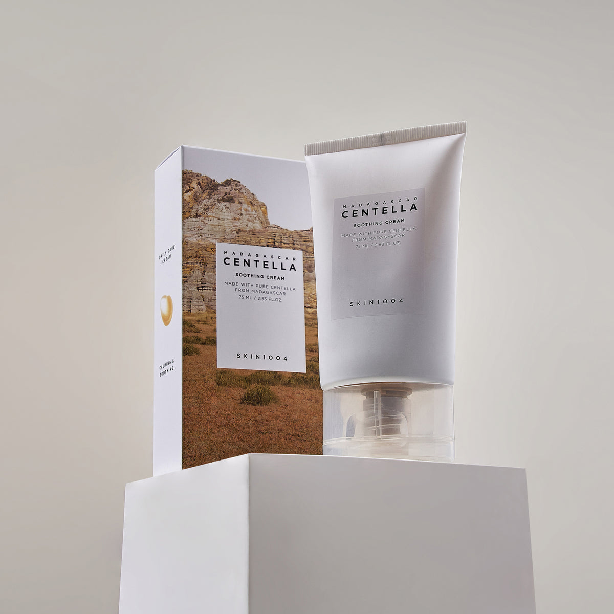 Eine Tube Madagascar Centella Soothing Cream steht neben der Schachtel auf einem weißen Sockel.