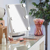 Schminktisch mit dem Glam & Groove Hollywood Bluetooth-Spiegel mit beleuchtetem Spiegel, Make-up-Pinseln, Tropfflasche, Rouge und Wimpernzange in Roségold.
