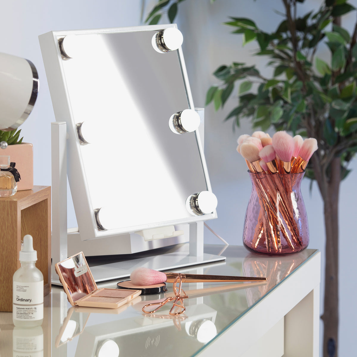 Schminktisch mit dem Glam & Groove Hollywood Bluetooth-Spiegel mit beleuchtetem Spiegel, Make-up-Pinseln, Tropfflasche, Rouge und Wimpernzange in Roségold.