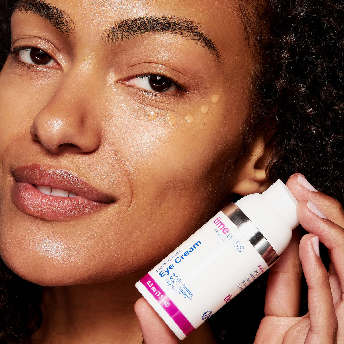 Frau mit aufgetragener Augencreme hält Timeless Skincare Eye Cream gegen Augenringe mit Hyaluron und Haloxyl™.