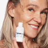Eine Frau trägt mit einer Pipette Serum aus einer Flasche Hyaluronsäure-Serum auf ihr Gesicht auf.