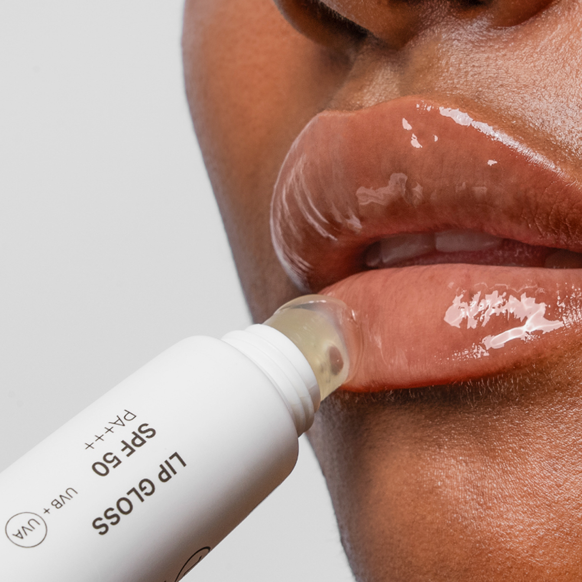 Nahaufnahme glänzender Lippen, während eine Person Lipgloss SPF50 aus einer Tube aufträgt.