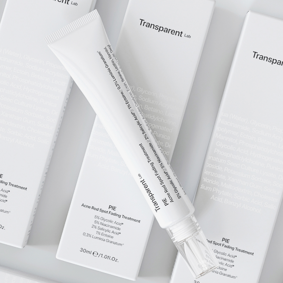Eine weiße Tube P.I.E Acne Red Spot Fading Treatment, liegt schräg auf drei Verpackungen auf weißem Hintergrund.