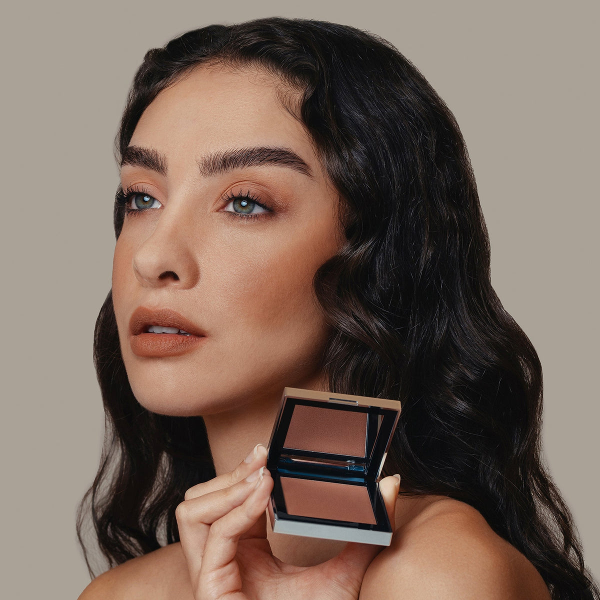 Eine Frau hält den geöffneten Skin Mate Compact von Mesauda Beauty in der Nähe ihres Gesichts.
