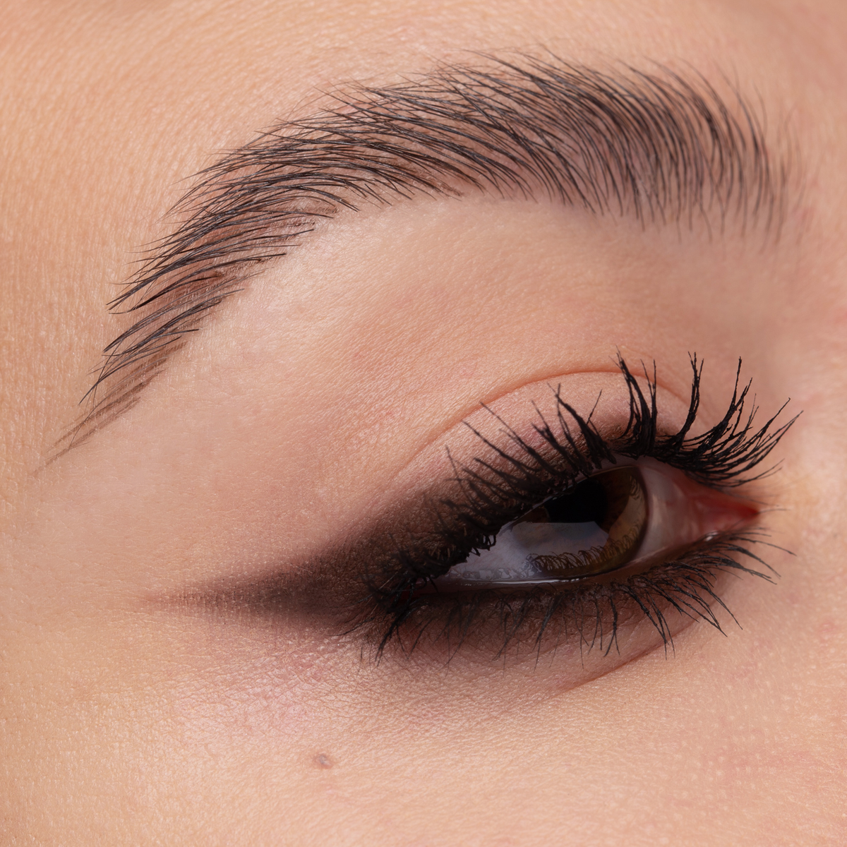 Nahaufnahme eines braunen Auges mit voluminösen Wimpern, dramatisches dunkelbraunen Smokey-Eye-Make-up, kreiert mit Cupid’s Arrow Longwear Stylo.
