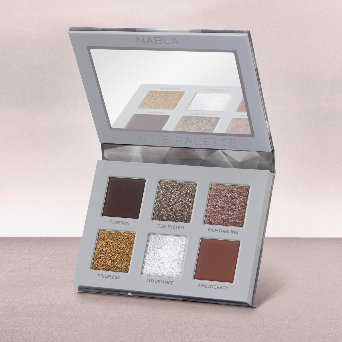 Geöffnete NABLA Cutie Palette „Platinum“ mit sechs Lidschatten in matten und schimmernden Silber-, Gold- und Brauntönen auf rosa Untergrund.