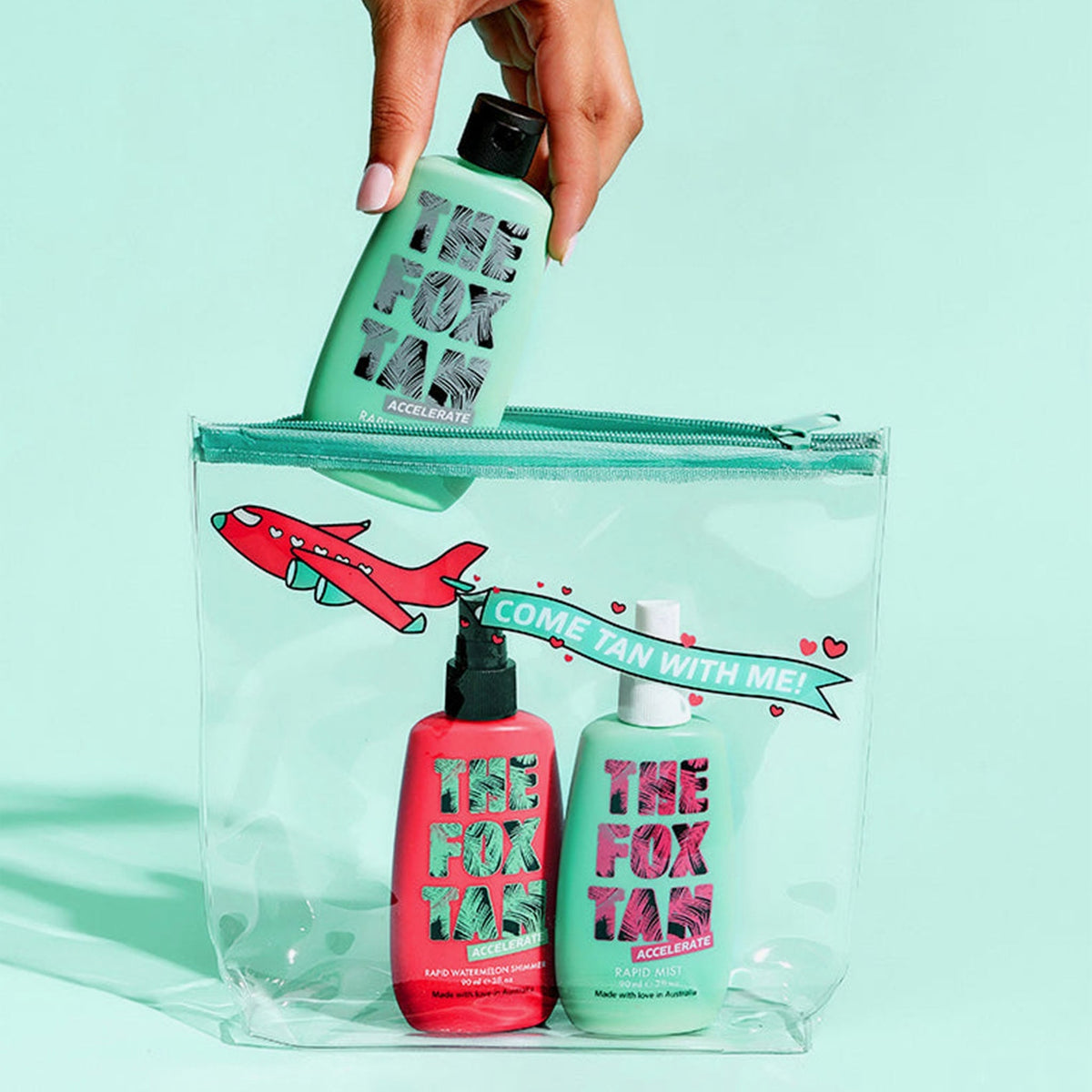 Eine Hand hält eine grüne Flasche über einer durchsichtigen Tasche mit roten und türkisen Flaschen, die mit „The Jet Setter“ beschriftet sind und ein rotes Flugzeugmotiv aufweisen.