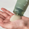 Eine Person gibt Heartleaf Quercetinol Pore Deep Cleansing Foam aus einer grünen Flasche auf die Handfläche.