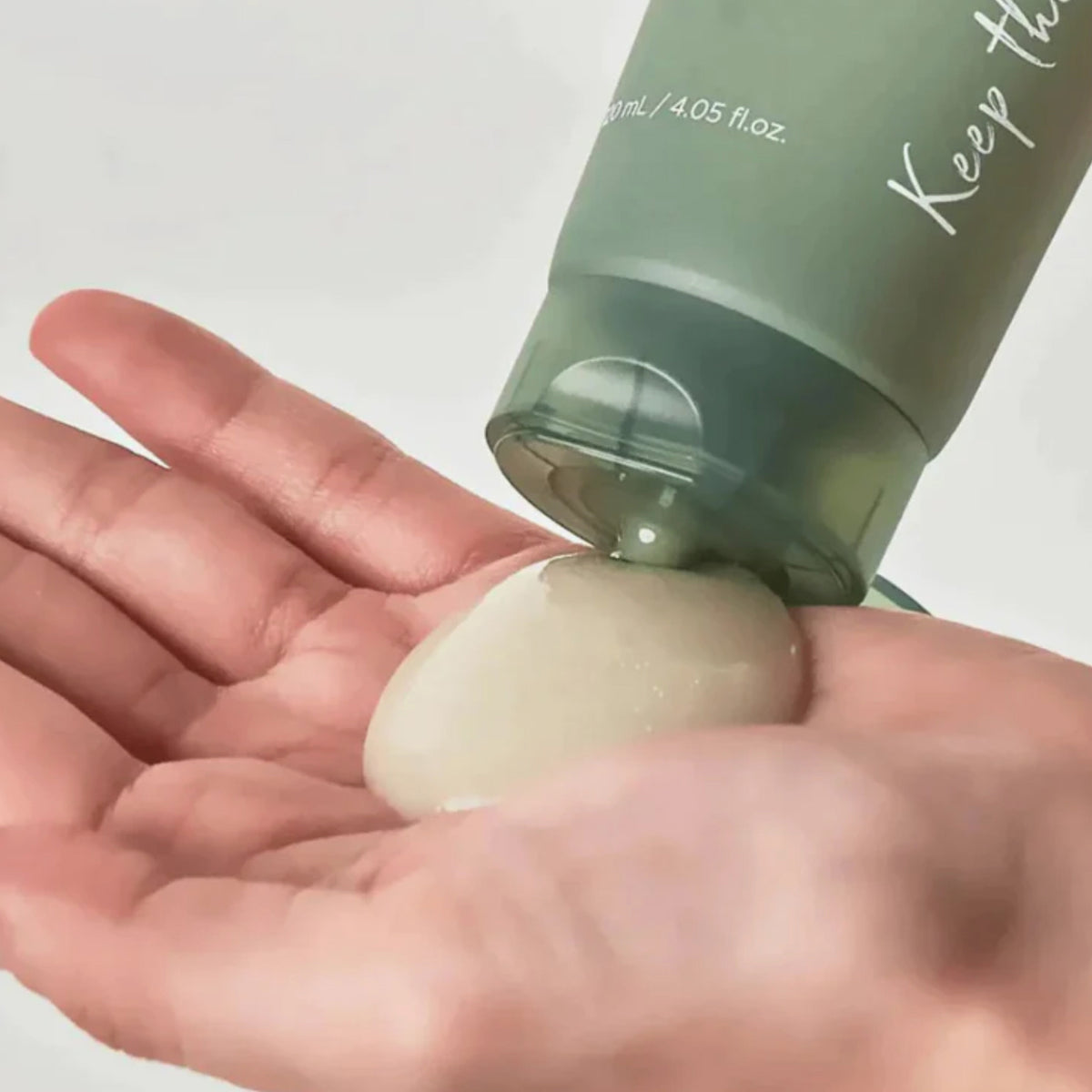 Eine Person gibt Heartleaf Quercetinol Pore Deep Cleansing Foam aus einer grünen Flasche auf die Handfläche.