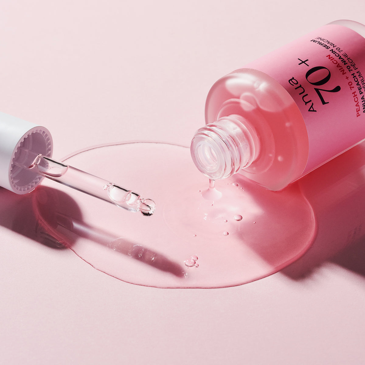 Eine Flasche Peach 70 % Niacinamide Serum mit rosa Flüssigkeit, die mit einer Pipette auf eine hellrosa Oberfläche gekippt wurde.