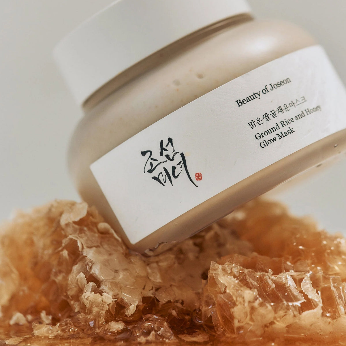 Nahaufnahme des Ground Rice and Honey Glow Mask-Tiegel auf einer Honigwabe.