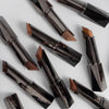 Mehrere Shapestick Bronze & Define in verschiedenen Braun-Tönen sind auf einer weißen Oberfläche verteilt.