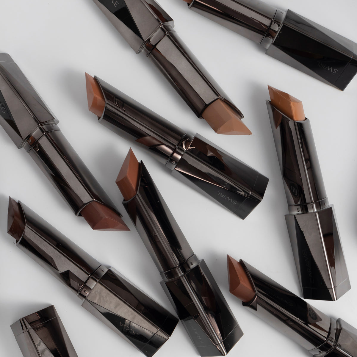 Mehrere Shapestick Bronze & Define in verschiedenen Braun-Tönen sind auf einer weißen Oberfläche verteilt.