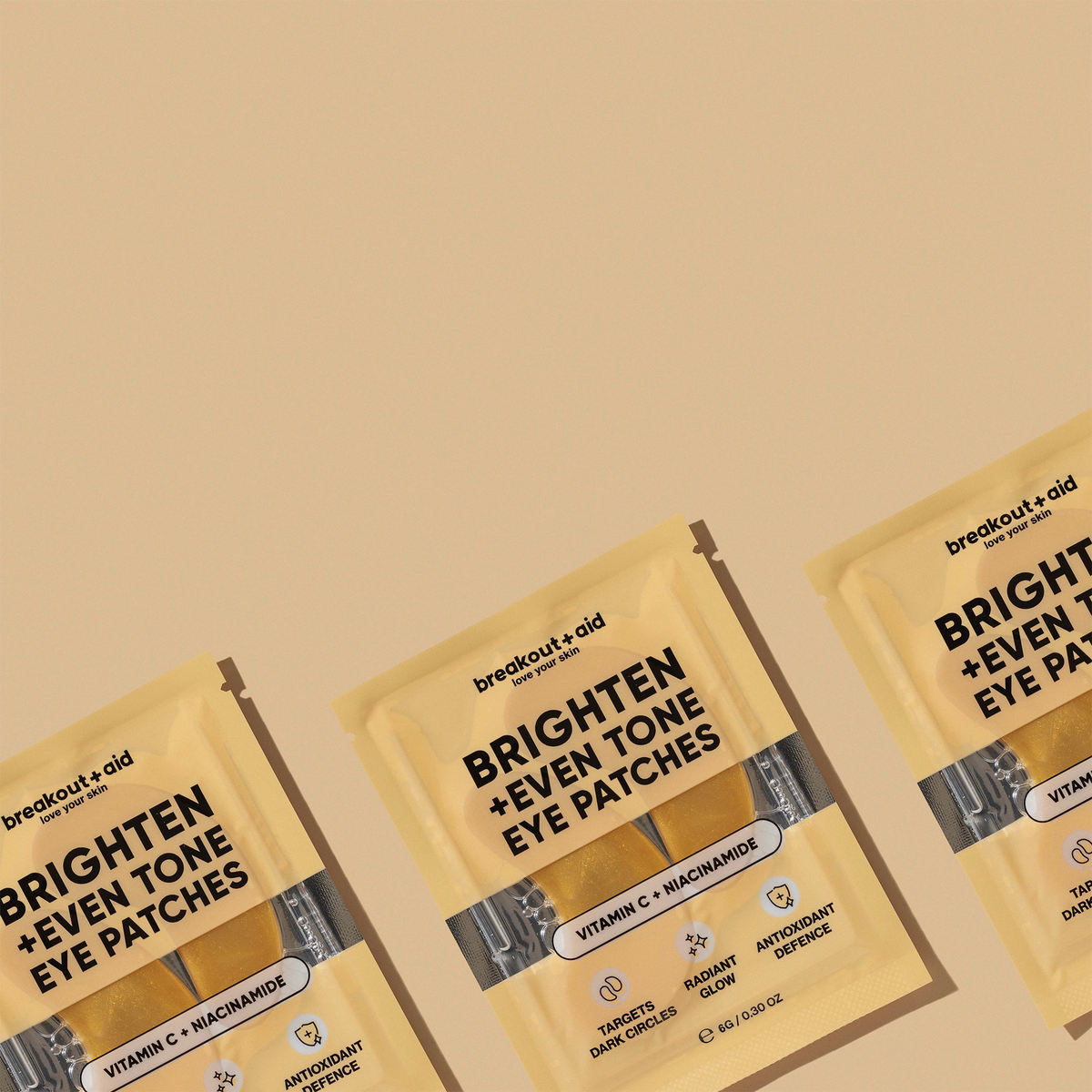 Drei goldgelbe Beutel mit Brighten + Even Tone – Hydrogel-Augenpads von breakout+aid, diagonal angeordnet.