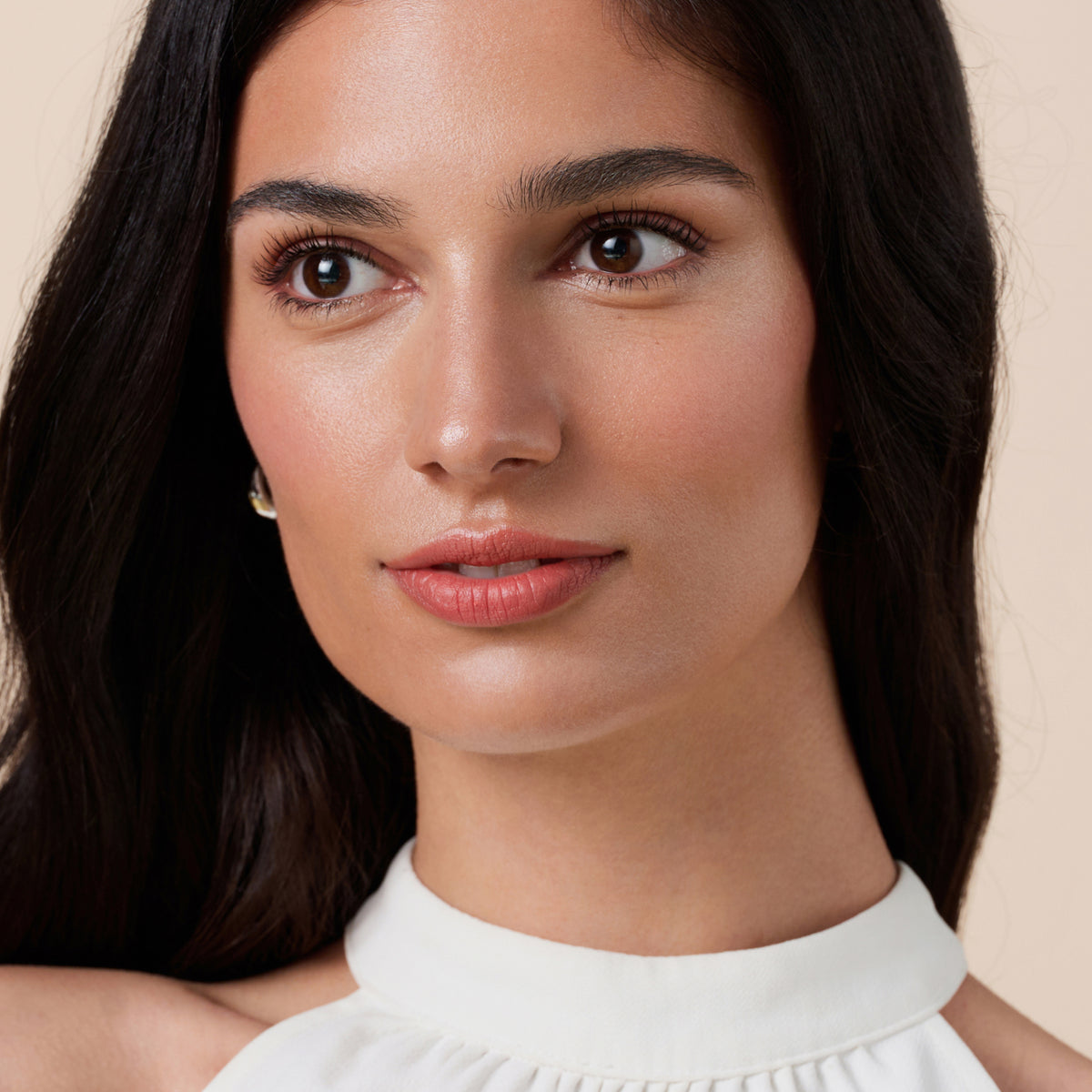 Eine Frau mit langem dunklem Haar in einem weißen Oberteil trägt den Soft Glam Filter Fluid 030 unter dem Make-up.