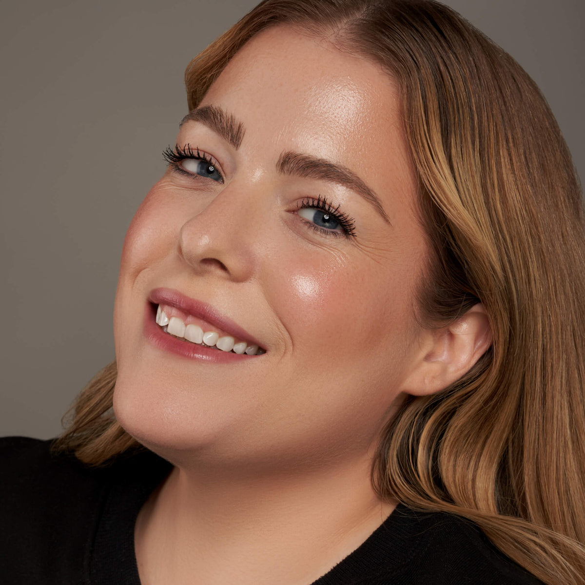 Lächelnde Frau mit strahlender Haut und natürlichem Make-up mit Danessa Myricks Beauty Dewy Cheek & Lip Palettes.